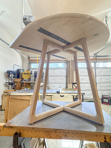 Oval cerused oak dining table photographed from below, showing the splayed leg joinery and structural cross-bracing