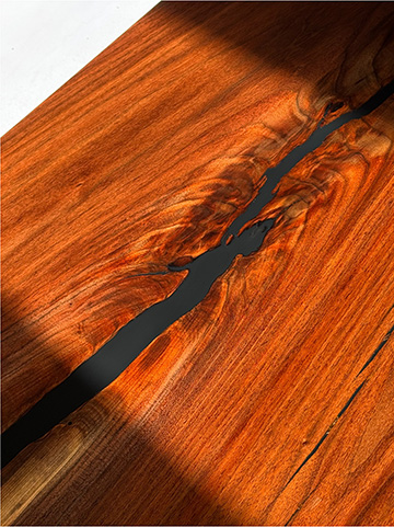 Macro detail of a walnut table top with a hand-poured black epoxy river filling a natural void in the figured grain