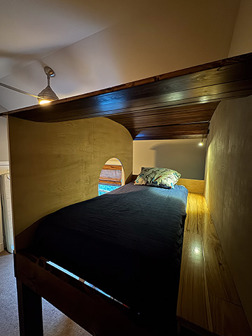 A built-in loft sleeping nook with a wood-clad ceiling, an arched window, and a custom platform bed framed into the architecture